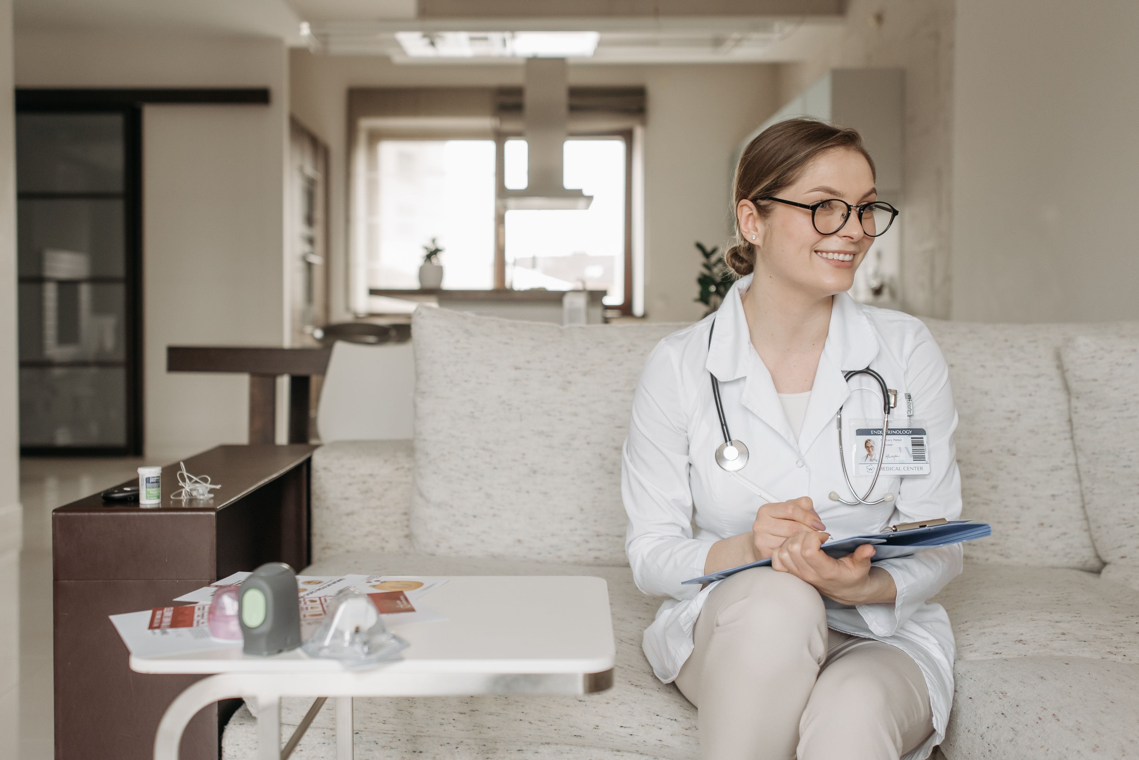 A smiling doctor with glasses and a stethoscope in a clinic room